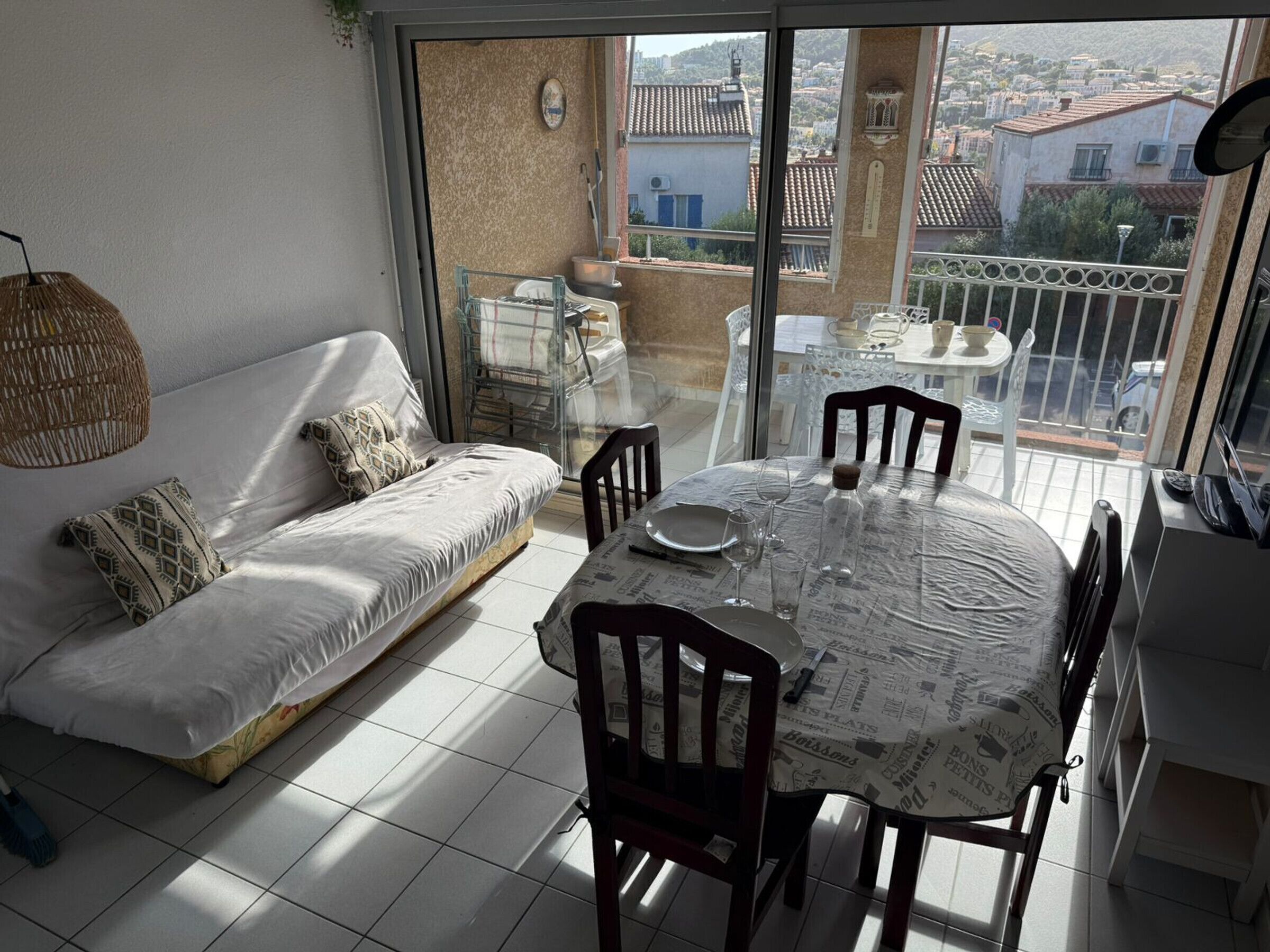 A balcony with a sofa, dining table, chairs, and a view of a town.
