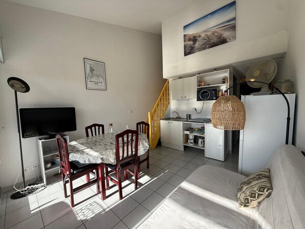 A compact living space with a dining area, kitchenette, and a TV.