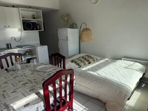A compact room with a kitchenette, a bed with patterned bedding, and a dining table set for two.