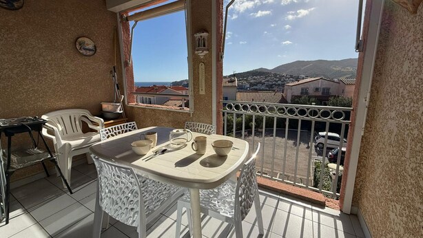 A balcony with a table and chairs, a view of a town, and a mountain in the distance.