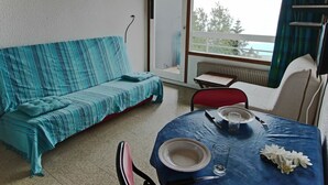 Ett rum med en soffa, ett matbord med tallrikar och ett glas, och en utsikt genom ett stort fönster.