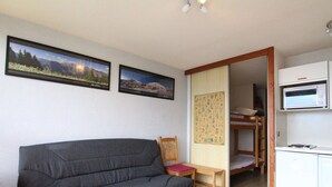 A compact living space with a sofa, a wooden table, a bunk bed, and a kitchenette. - Cozy 2-Room Apartment for 4 with South-Facing Balcony, Near Ski Lifts and Shops, L'Alpe d'Huez (Huez)