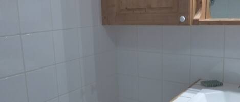 A bathroom with white tiles, a wooden cabinet, and a white sink with a green brush.