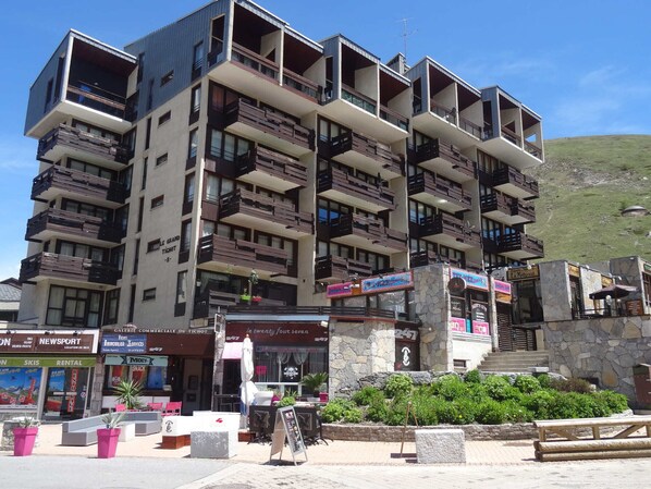 Un hotel de varios pisos con balcones, mobiliario exterior y fachada de piedra.