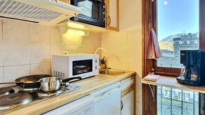 A compact kitchen with a microwave, stove, and sink. A window offers a view of a building and landscape. - Cozy 2-room apartment for 5 in Tignes, close to slopes and shops (Tignes)