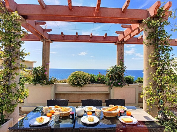 An outdoor dining area with a table set for breakfast, overlooking the sea.