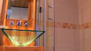 Un baño con lavamanos de cristal, mueble de madera y cabina de ducha con paredes de cristal.