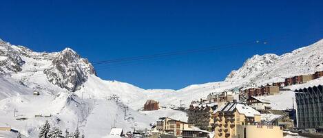 Uma cidade montanhosa coberta de neve, com mistura de edifícios tradicionais e modernos, um teleférico de esqui e um céu azul límpido.