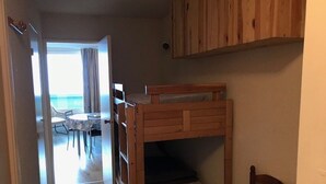 A compact room with a bunk bed, a wooden cabinet, and a view of a balcony with a table and chairs.