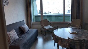 A room with a sofa, two chairs, a table, and a large window with a view of buildings.