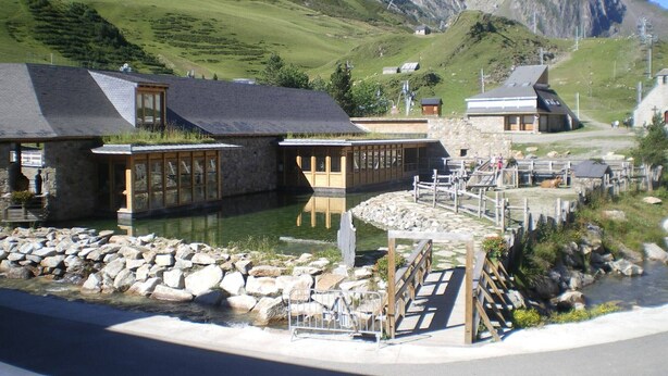 A mountain lodge with stone buildings, a wooden dock, and a clear view of the surrounding hills.