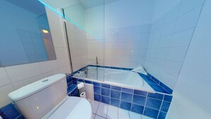 Un baño moderno con bañera de hidromasaje con mampara de vidrio, inodoro y zona de ducha.