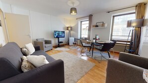 Una sala de estar moderna con un sofá, sillones, un televisor, una mesa de comedor con sillas y un amplio ventanal.