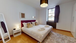 Una habitación de hotel moderna con una cama grande, mesitas de noche, un espejo y una ventana con cortinas.