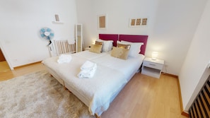 Un lit bien fait, avec du linge de lit blanc et un tapis moelleux, une table de chevet avec une lampe et un ventilateur fixé au mur.