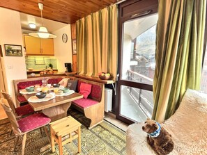 Un interior acogedor con zona de comedor, cocina y un amplio ventanal con cortinas.
