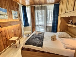 A wooden room with a bed, a chair, and a small stool.