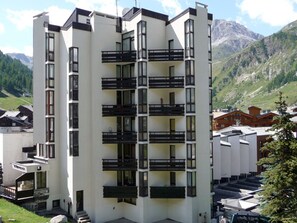 A modern multi-story building with balconies, set against a mountainous backdrop.