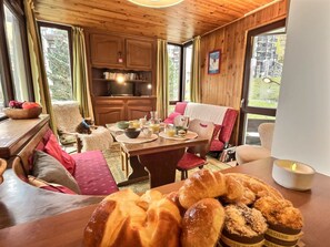 A cozy room with wooden walls, a dining table set with breakfast, a dog, and a view of greenery outside. - Comfortable apartment, village view - 5 guests (VAL D'ISERE)