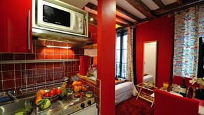 A compact kitchen with a microwave, stove, and sink. A bed and a dining area are visible in the adjacent room. - E3GG Travel the world (Paris)