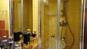 A bathroom with yellow tiled walls, a glass shower enclosure, and a variety of toiletries on a shelf. - E3GG Travel the world (Paris)
