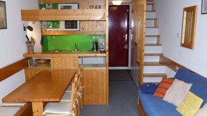 Una habitación compacta con una mesa de madera, sillas, un sofá y una zona de kitchenette.
