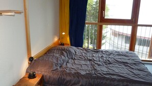 Un dormitorio con cama, mesita de noche de madera, lámpara y ventana con cortinas.