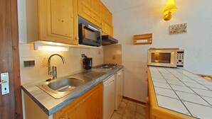 A compact kitchen with wooden cabinets, a stainless steel sink, a stove, and two microwaves.