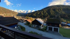 A mountain village with traditional buildings, a road, and snow-capped mountains in the background.