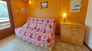 A bedroom with a bed, wooden walls, a wooden cabinet, and a window with a view of trees.