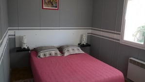 A bedroom with a bed, pillows, a nightstand, a picture frame, and a window. - Gîte au milieu des Vignes G286 (Vidauban)