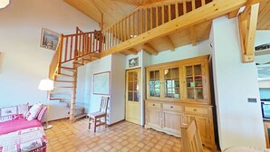 Ein geräumiges Zimmer mit einer Holztreppe, einem Essbereich mit Schrank und einem Bett mit gemustertem Überwurf.