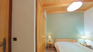 Ein Schlafzimmer mit Holzbalkendecke, einem Bett, einem Nachttisch, einer Lampe und einer Wandleuchte.