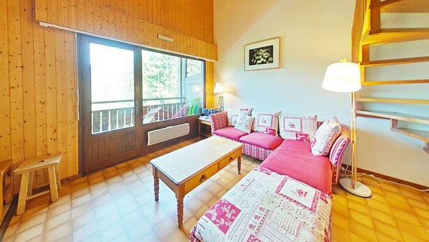 Ein gemütliches Zimmer mit Holzwänden, einem großen Fenster, einem Bett mit Steppdecke, einer Couch mit gemusterten Kissen und einem kleinen Tisch.
