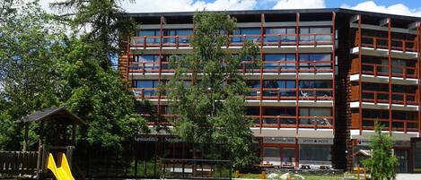 Un immeuble à plusieurs étages doté de balcons, une aire de jeux avec un toboggan et une zone piétonne aux couleurs vives.