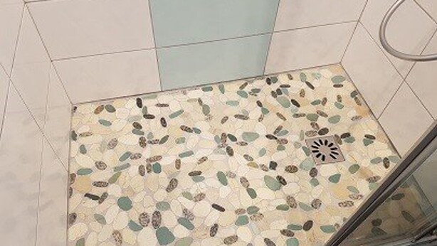 A shower with a mosaic floor and a glass door.