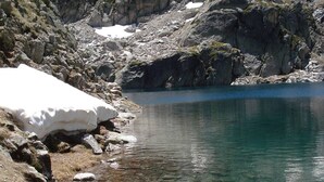 A clear mountain lake with rocky shores and snow patches.