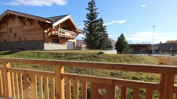 A wooden building with a balcony, surrounded by a grassy area and trees.