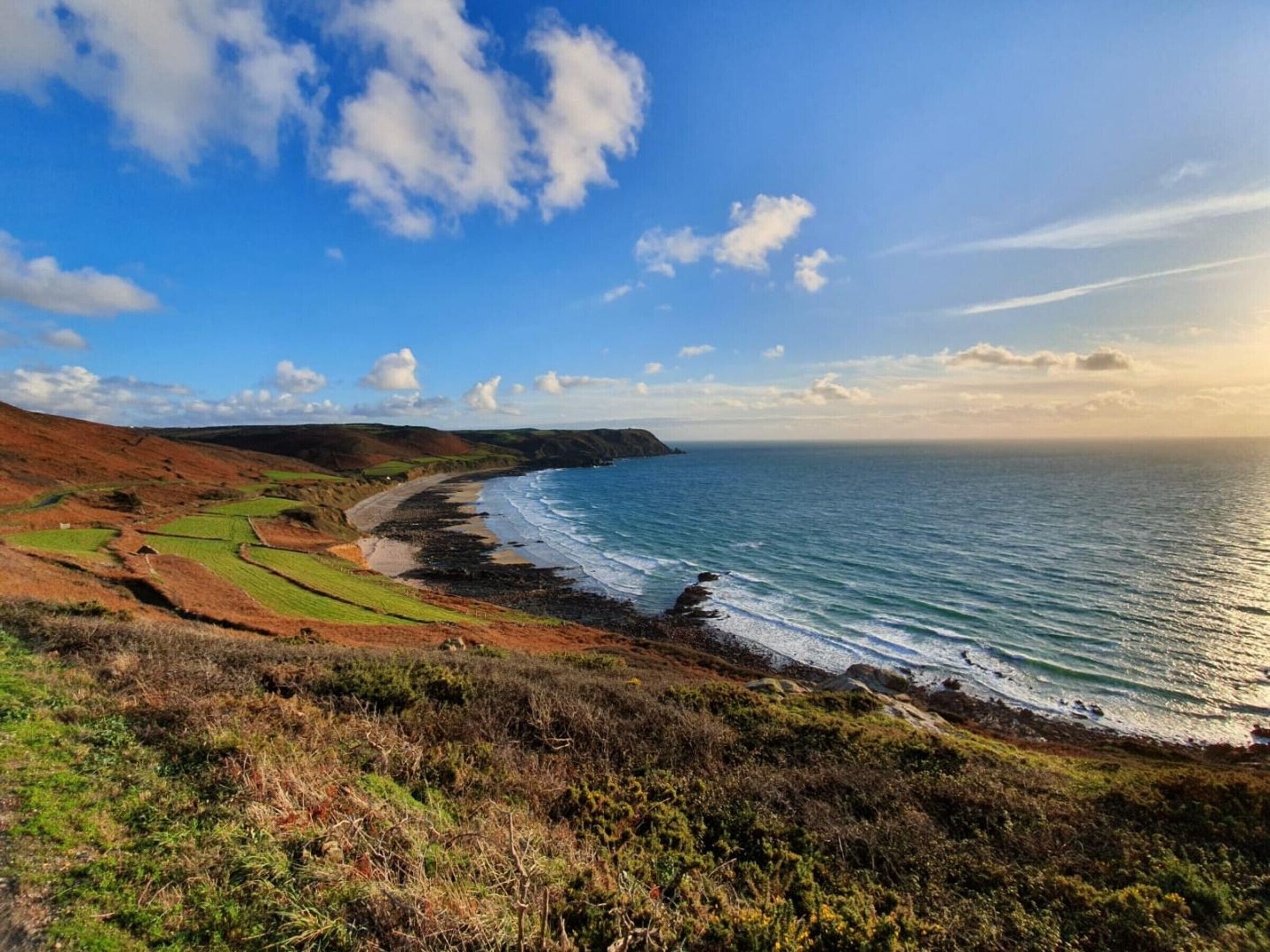 A coastal landscape with green fields, a beach, and a rocky shoreline.