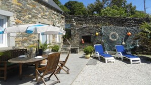 A stone building with a patio area featuring a table and chairs, a covered umbrella, and two lounge chairs.