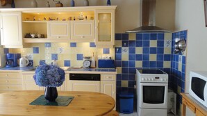 A kitchen with white cabinets, a blue and yellow tiled backsplash, a white stove, and a wooden table with a vase of flowers.