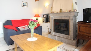 A living room with a stone fireplace, a sofa with red cushions, a wooden coffee table, and a television.
