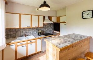 Een kleine keuken met houten kastjes, een gootsteen, een koffiezetapparaat en een klok aan de muur.