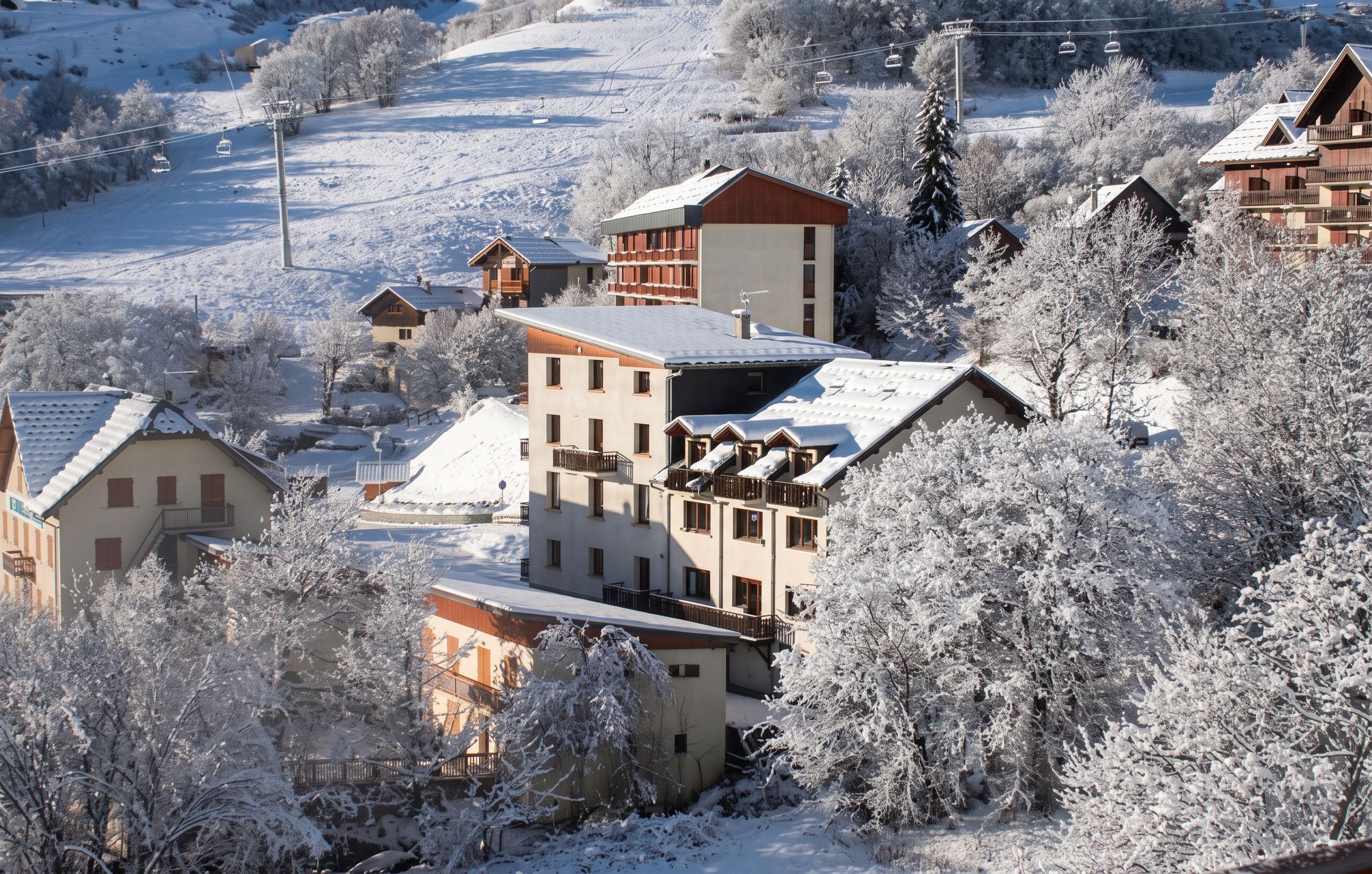 Un pueblo cubierto de nieve con edificios de estilo chalete tradicional, un telesilla y una vista despejada del paisaje nevado circundante.