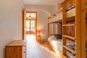 Une chambre avec des lits superposés, une commode en bois, une table avec une lampe et une vue sur un balcon.