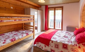 Une chambre avec des lits superposés, un lit simple avec une couverture rouge, une fenêtre avec un rideau rouge et un radiateur.