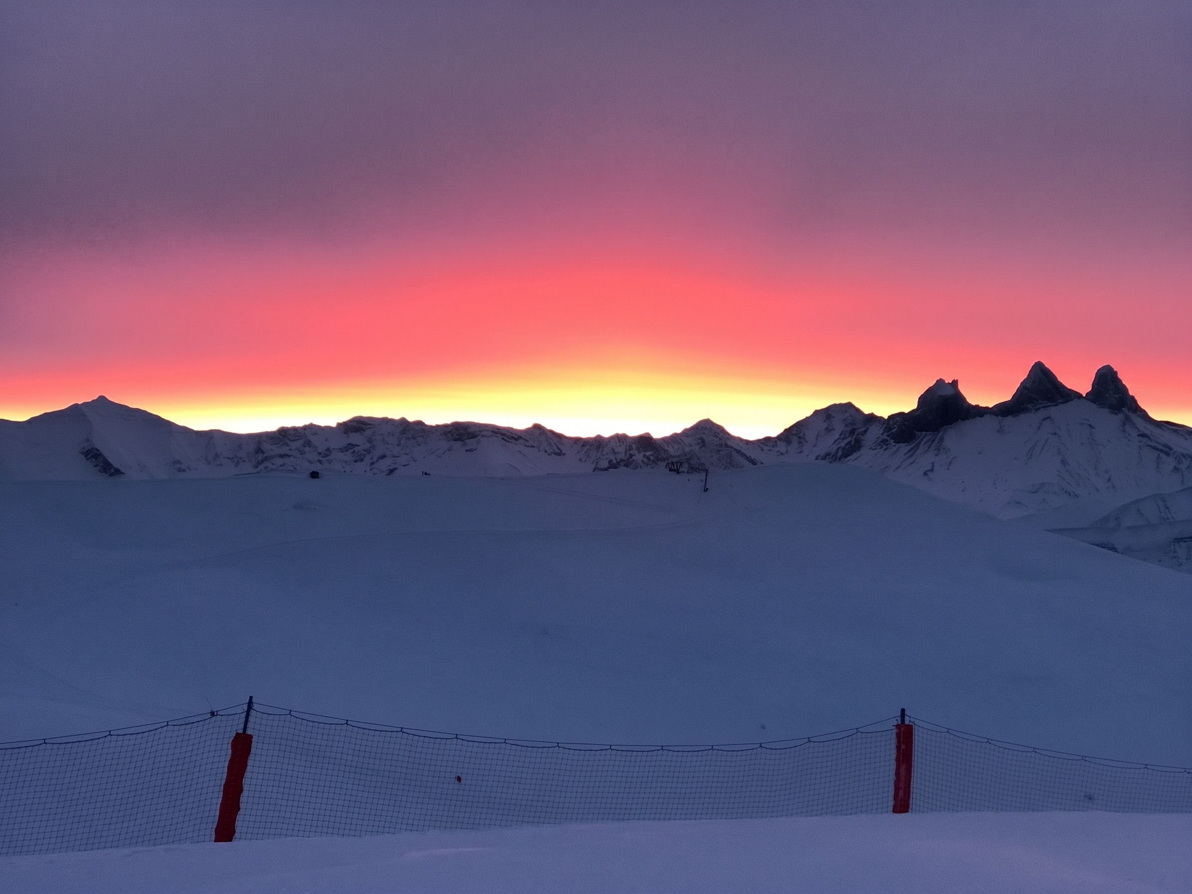 Un paysage enneigé, avec une clôture au premier plan et une chaîne de montagnes en arrière-plan.