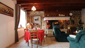 Un salon chaleureux avec une cheminée en pierre, un coin repas avec une table et des chaises, et un canapé vert.