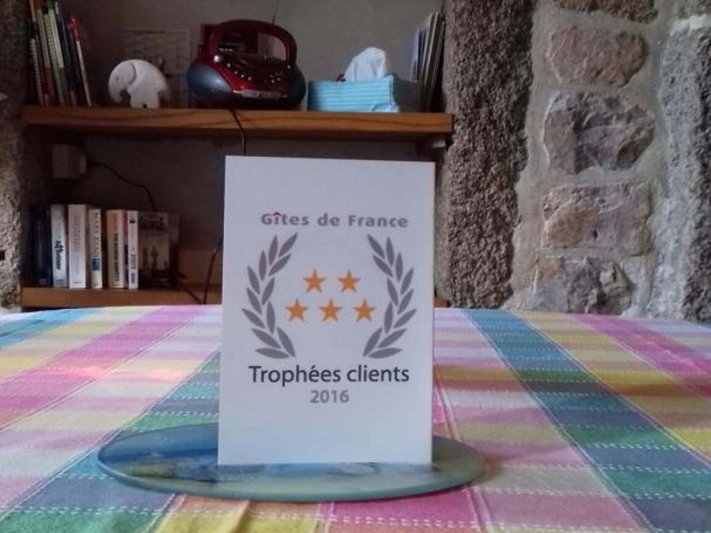 Un letrero con la inscripción 'Gîtes de France Trophées clients 2016' sobre una mesa cubierta con un mantel colorido.