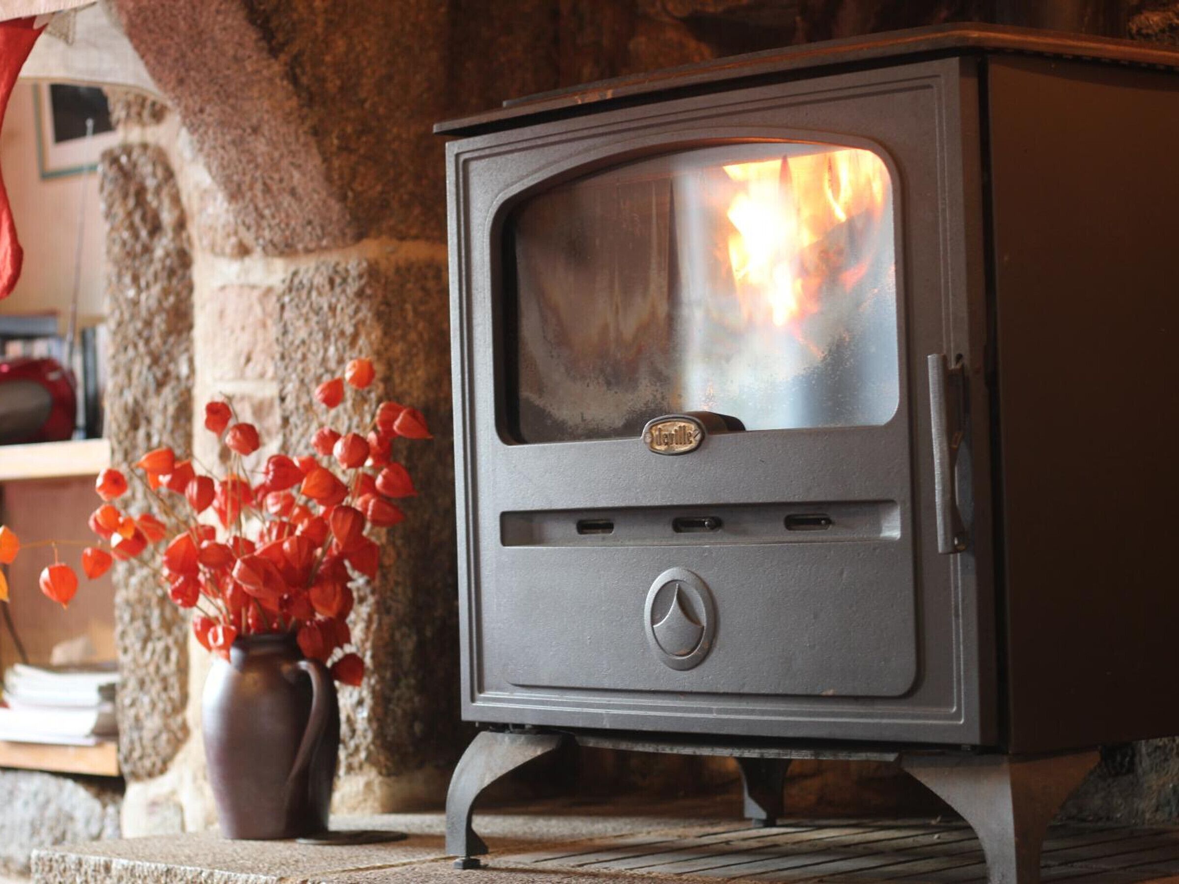 A wood-burning stove with a glass door, placed in a stone-walled room.
